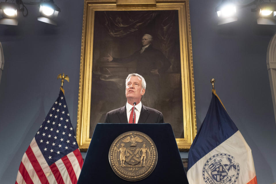 FILE - In this Aug. 2, 2019 file photo, New York Mayor Bill de Blasio speaks at a news conference in New York. The New York City Seal appears on the podium that de Blasio speaks from as well as on one of the flags behind him. De Blasio said on Monday, July 27, 2020 that he would be in favor of re-examining if the city seal holds up to contemporary scrutiny after a founding member of a Native American group said the Native American man shown on the seal is 