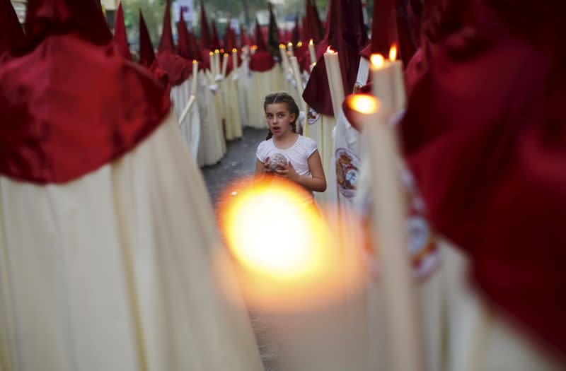 FILE PHOTO: A girl holds ball of wax between penitents of La Lanzada brotherhood during Holy Week in the Andalusian capital of Seville