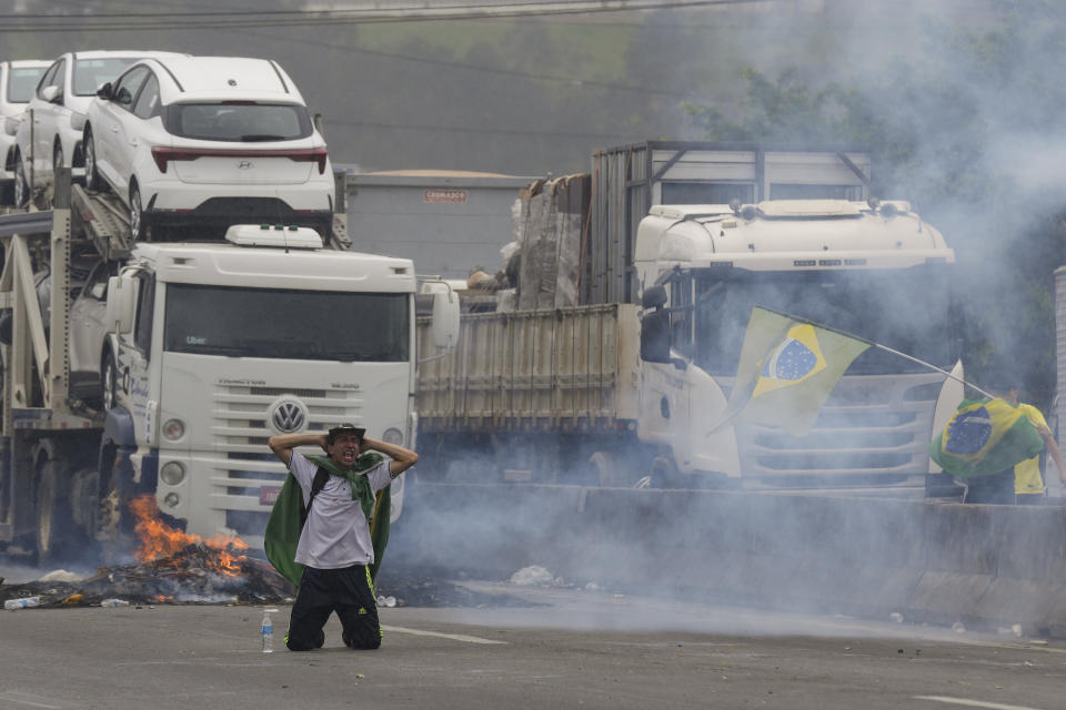 A protester kneels with his hands behind his head as riot police launch tear gas at truckers blocking a highway in protest against President Jair Bolsonaro's loss in the country's presidential runoff election, in Embu das Artes, outskirts of Sao Paulo, Brazil, Tuesday, Nov. 1, 2022. Since the former President Luiz Inacio Lula da Silva's victory Sunday night, many truck drivers have jammed traffic in areas across the country and said they won’t acknowledge Bolsonaro’s defeat. Bolsonaro hasn’t spoken publicly since official results were released roughly 36 hours ago, nor phoned da Silva to concede. (AP Photo/Andre Penner)