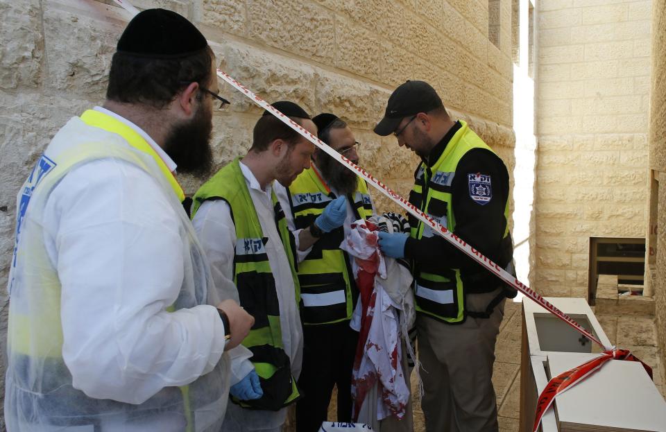 A member of the Israeli Zaka emergency response team holds bloody clothes and a prayer shawl at the scene of an attack at a Jerusalem synagogue