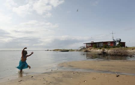 A young girl plays in the water in front of the last house remaining on Cedar Island off the coast of Wachapreague, Virginia July 20, 2014. Kevin Lamarque