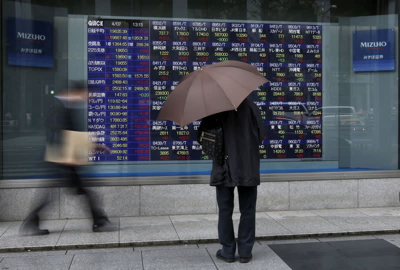 FILE PHOTO: A man holding an umbrella looks at an electronic stock quotation board outside a brokerage in Tokyo