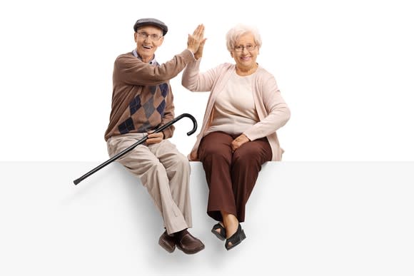 A senior couple sitting on a bench give each other a high five.