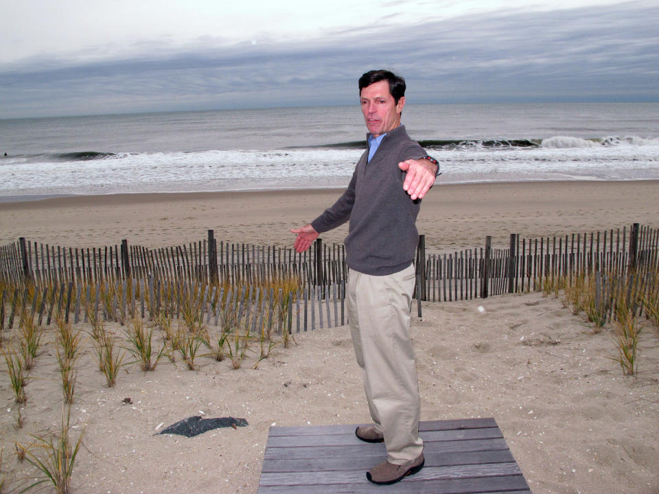 FILE- In this Nov. 25, 2014, file photo, Thacher Brown speaks at the edge of the dune behind his home in Bay Head, N.J. Brown is one of a group of oceanfront homeowners who spent $5 million to install their own sand-covered rock wall to protect Bay Head from future storms, and who opposed then-Gov. Chris Christie's plan to widen beaches and build dunes along the state's coastline. He says it's unfair that some shore towns were not required to build dunes after Superstorm Sandy. (AP Photo/Wayne Parry, File)