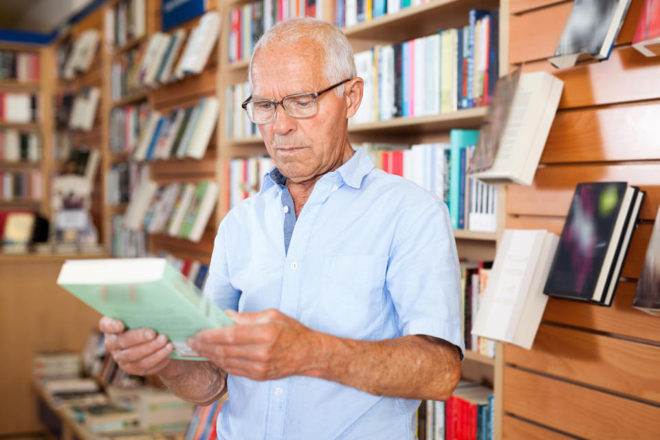 Senior man holding book in bookstore.