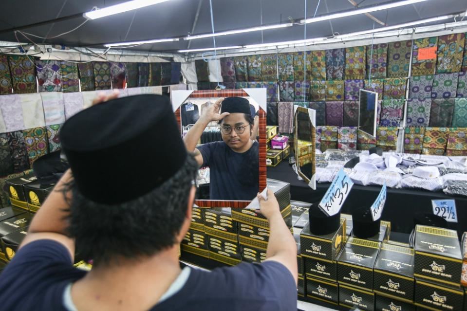 A customer is seen trying on a songkok for the Hari Raya Aidilfitri celebration at Mydin Meru in Ipoh April 17, 2023. — Picture by Farhan Najib