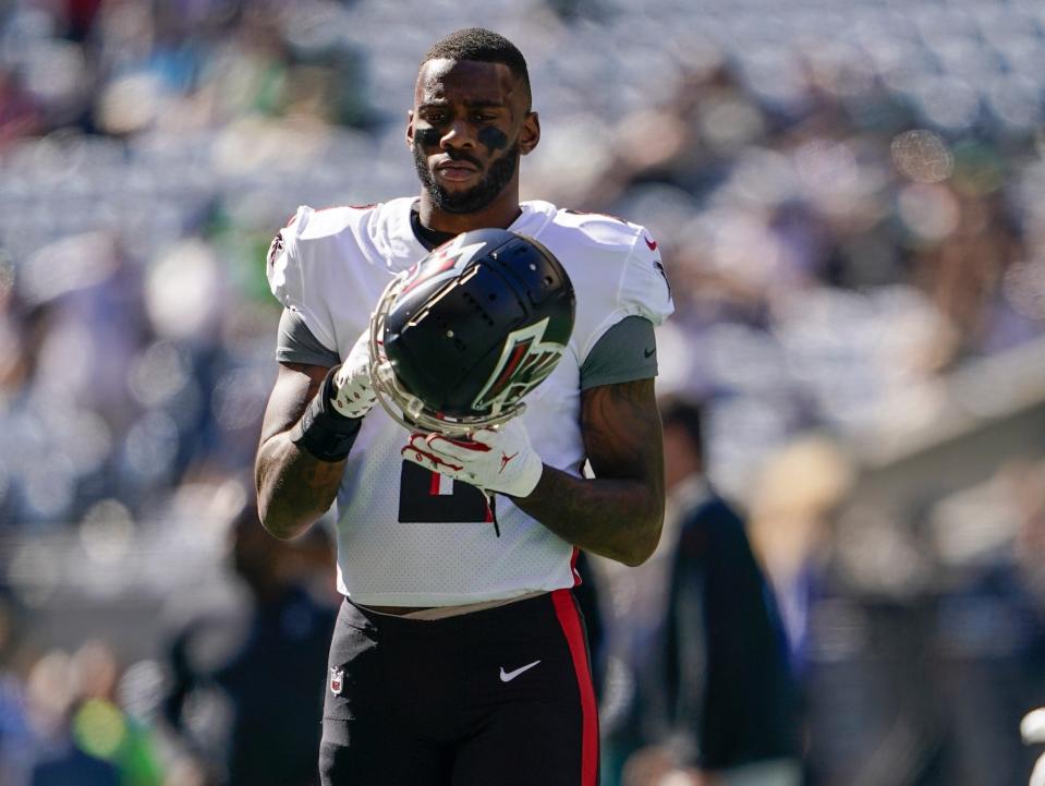 Kyle Pitts holds his helmet while standing on the field during a Falcons game.