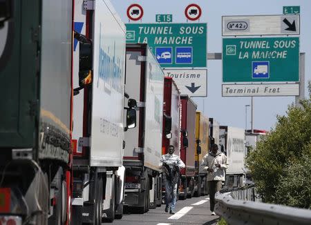 Migrants walk near trucks blocked on a road which leads to the Channel Tunnel terminal in Coquelles near Calais, northern France, June 30, 2015. REUTERS/Vincent Kessler