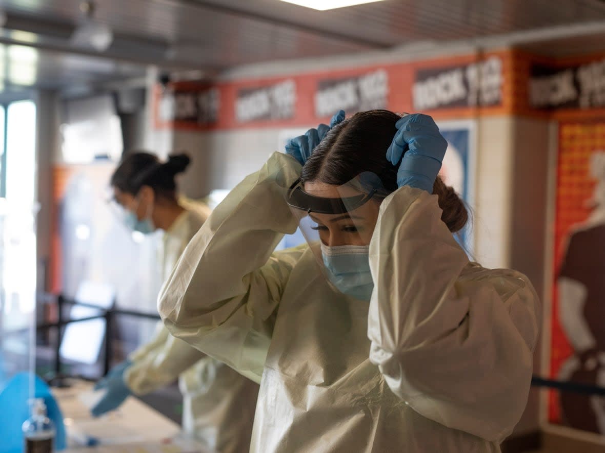 Volunteer Montana Ledoux puts on PPE at the Saskatoon Tribal Council-run vaccination clinic inside SaskTel centre in Saskatoon, Sask., on April 15, 2021. (Kayle Neis/The Canadian Press - image credit)