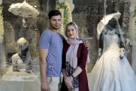 In this July 3, 2019 photo, newly married Iranian couple Mohammad Davoodi, 28, and his wife Mahsa Asadzadeh, 20, pose for a photo in front of a wedding dress shop in downtown Tehran, Iran. Iran’s large middle class has been hit hard by the fallout from unprecedented U.S. sanctions, including the collapse of the national currency. Perhaps most devastating has been the doubling of housing prices. More newlyweds move in with their families to save money. (AP Photo/Ebrahim Noroozi)