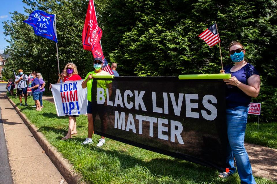 Supporters of President Donald Trump and protesters hold banners as they wait for the motorcade of President Trump outside the Trump National Golf Club in Sterling, Va., Sunday.