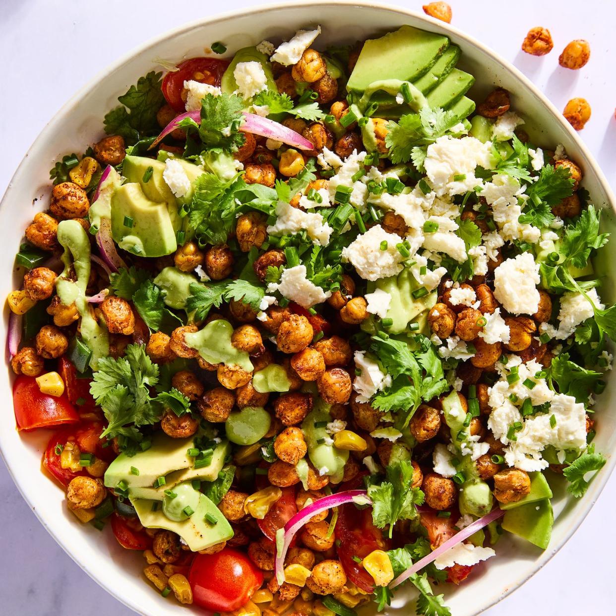 salad tossed with crispy chickpeas, avocado slices, red onions, sliced tomatoes, corn, and topped with herbs and cheese