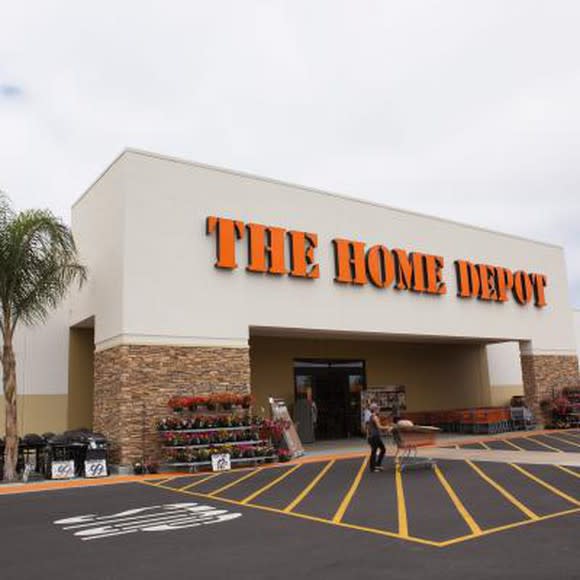 The front door of a Home Depot viewed from the parking lot. A customer is pushing a cart through the front door.