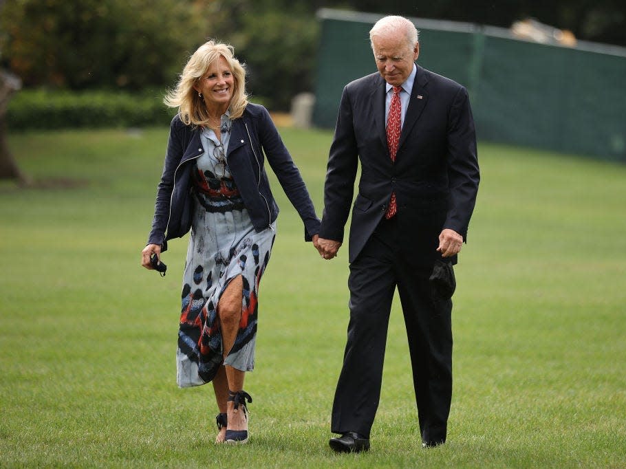 President Joe Biden and first lady Dr. Jill Biden walk on the White House lawn holding hands.