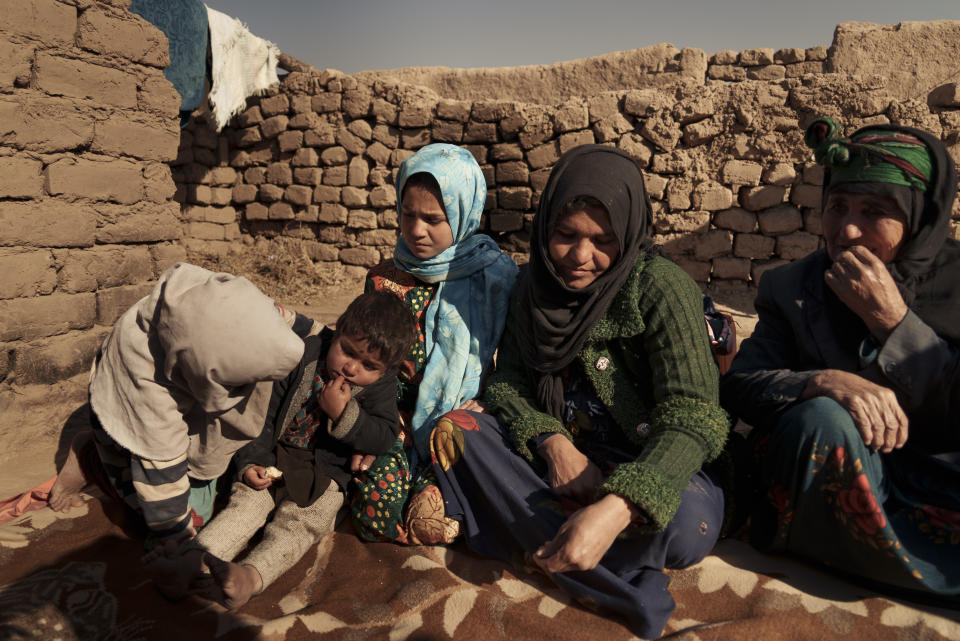 Aziz Gul, second from right, and her 10-year-old daughter Qandi, center, sit outside their home with other family members, near Herat, Afghanistan. Dec. 16, 2021. Qandi's father sold her into marriage without telling his wife, Aziz, taking a down-payment so he could feed his family of five children. Without that money, he told her, they would all starve. He had to sacrifice one to save the rest. (AP Photo/Mstyslav Chernov)