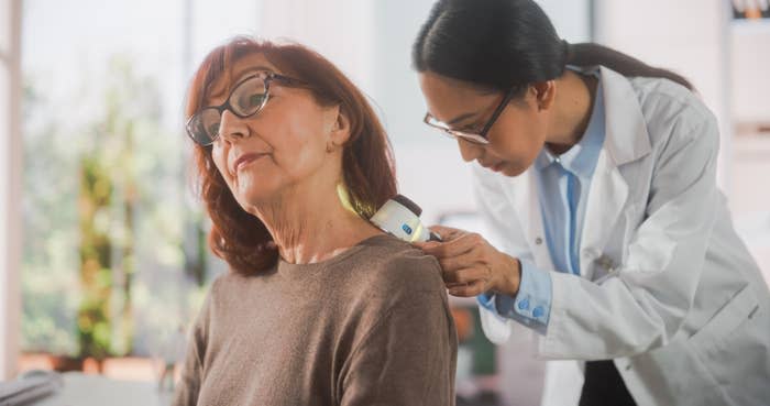 Portrait of a Young Dermatologist Using a Medical Magnifying Glass to Inspect any Damages on the Skin of a Senior Patient During a Health Check Visit to a Clinic. Doctor Working in Hospital