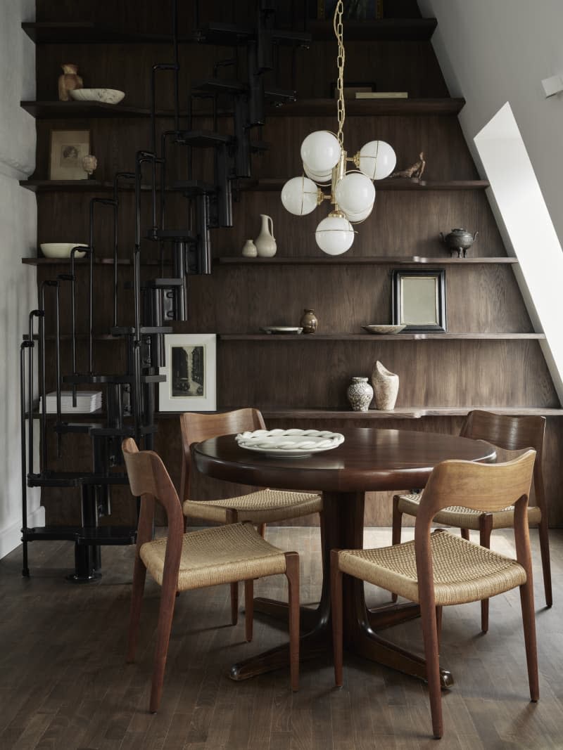 wood wall with exposed shelving, angled wall with large cut outs for windows with orb lighting fixture above dining table