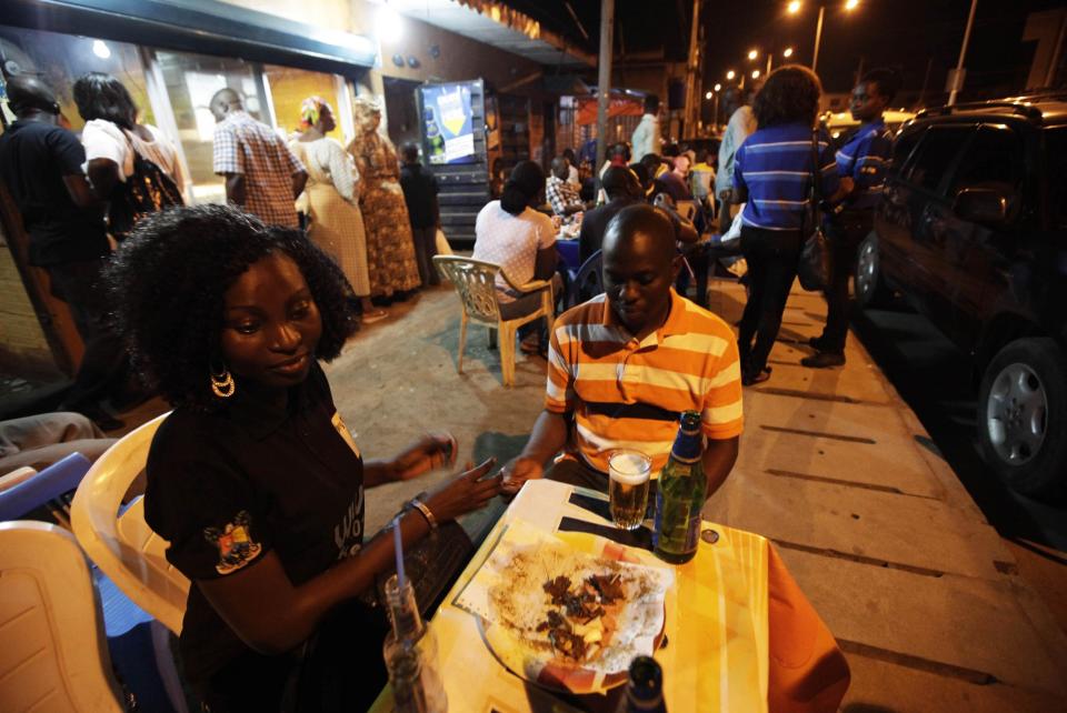 In this photo taken on Saturday, Oct. 20, 2012, people drink beers and eat suya at night at a "Supa Suya" eatery in Lagos, Nigeria. As night falls across Nigeria, men fan the flames of charcoal grills by candlelight or under naked light bulbs, the smoke rising in the air with the smell of spices and cooking meat. Despite the sometimes intense diversity of faith and ethnicity in this nation of 160 million people, that thinly sliced meat called suya, is eaten everywhere. (AP Photo/Sunday Alamba)