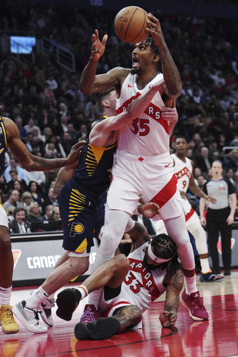 Toronto Raptors center Malik Williams (35) is wrapped up by Indiana Pacers guard T.J. McConnell, left, as Raptors guard Gary Trent Jr. (33) protects himself during the second half of an NBA basketball game in Toronto on Tuesday, April 9, 2024. (Nathan Denette/The Canadian Press via AP)
