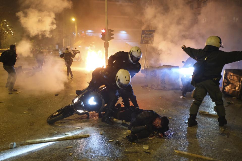 A policeman lays injured on the road after an attack by protesters as his colleagues try to help him during clashes in Athens, Tuesday, March 9, 2021. Severe clashes broke out Tuesday in Athens after youths protesting an incident of police violence attacked a police station with petrol bombs, and severely injured one officer. (AP Photo/Aggelos Barai)