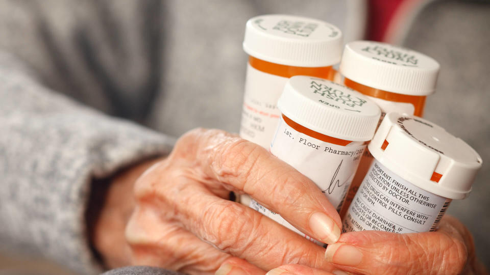 Senior citizen female holding bottles of prescription medicine sitting in a wheelchair.