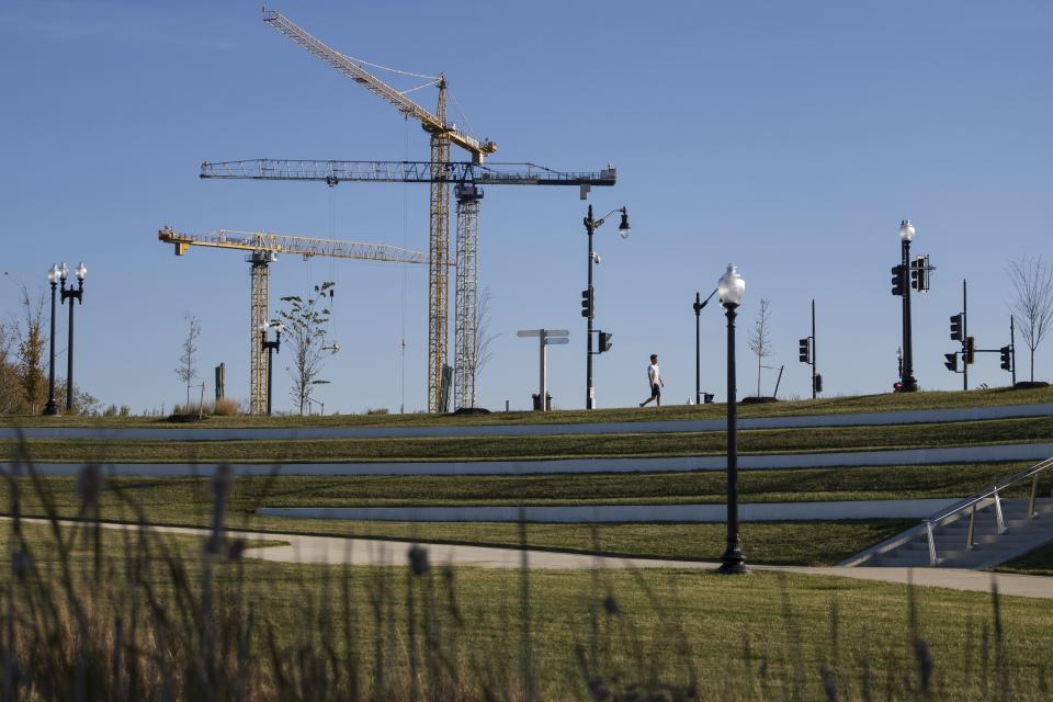 A pedestrian walks near the Fredrick Douglass Bridge on Thursday, Nov. 16, 2023, at Anacostia Park in Washington. Constriction cranes have been increasingly visible as more residential buildings have been developed throughout the Anacostia section of Washington. (AP Photo/Tom Brenner)