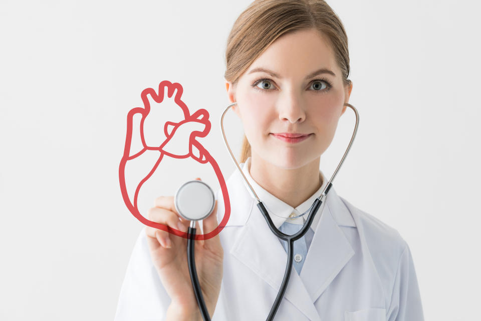 Doctor with a stethoscope held up to an image of a heart checking heart health.