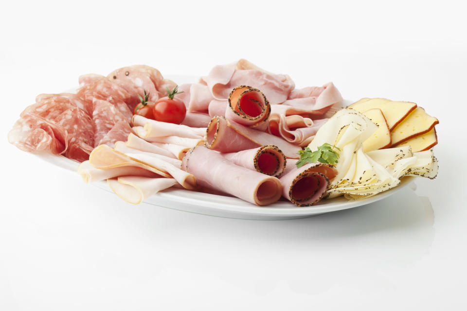 Variety of meat and cheese slices in plate on white background