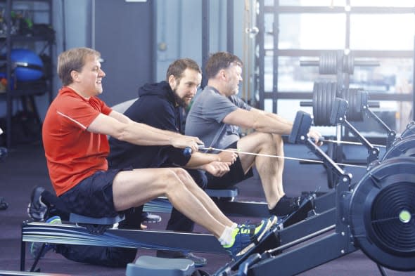 Men group weight training class working with rowing machine in a health club facility.