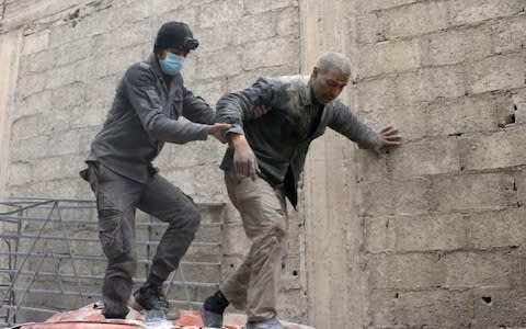 A Syrian rescuer helps a man at the site of Syrian government bombardments in Douma - Credit: HAMZA AL-AJWEH/AFP