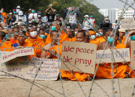 Buddhist monks pray and hold placards behind a wire barricade at Dhammakaya temple, in Pathum Thani province, Thailand February 23, 2017. REUTERS/Chaiwat Subprasom