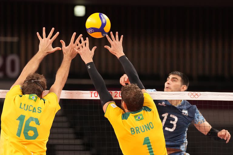 Lucas Saatkamp de Brasil y Bruno Mossa Rezende intentan bloquear un balón del argentino Ezequiel Palacios, durante un partido de la ronda preliminar del grupo B de voleibol masculino, en los Juegos Olímpicos de Verano de 2020, el lunes 26 de julio de 2021 en Tokio, Japón. (Foto AP / Frank Augstein)