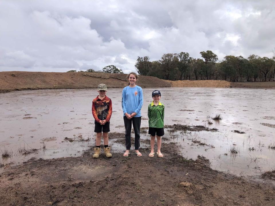 Ms Groth's children Brianna, 14, Jayden, 10, and Macklin, 8, are seen smiling as they stand in front of the quickly rising dam. Source: Lindsay Groth