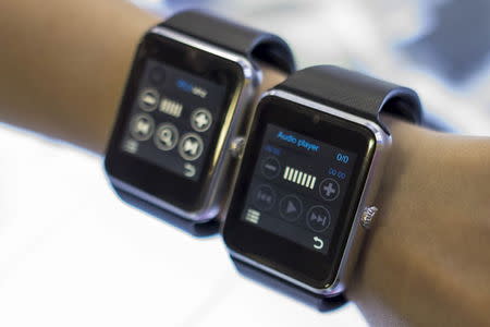 A salesman poses with two Apple Watch look-alike devices, made by a Chinese manufacturer, at a mall selling electronic products in China's southern city of Shenzhen, April 8, 2015. REUTERS/Tyrone Siu