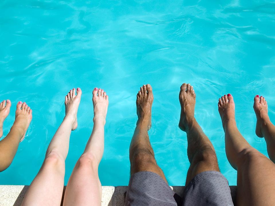 People dangle their legs over the edge of a swimming pool.