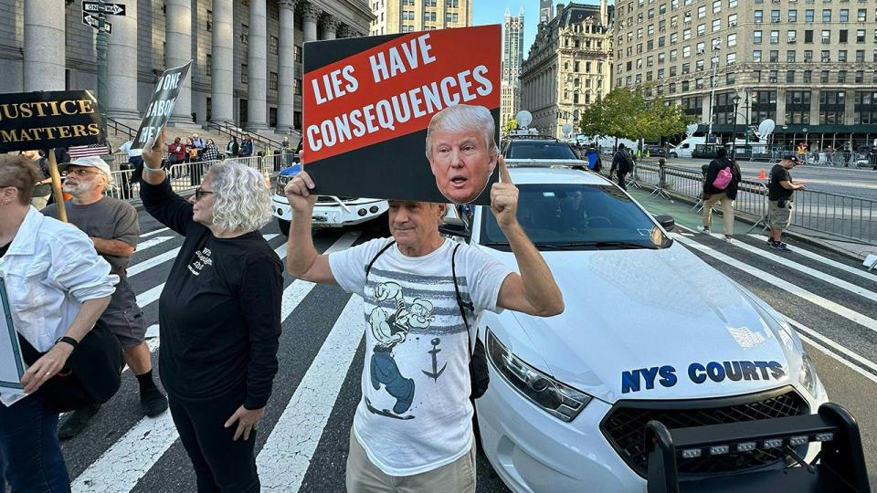 Protestors hold placards before the arrival of former President Donald Trump to New York State Supreme court for the start of the civil fraud trial against him on October 2, 2023 in New York City. Donald Trump faces fresh legal danger as a civil fraud trial against the former president and two of his sons begins in New York, threatening the Republican frontrunner's business empire as he campaigns to retake the White House with four criminal cases looming.