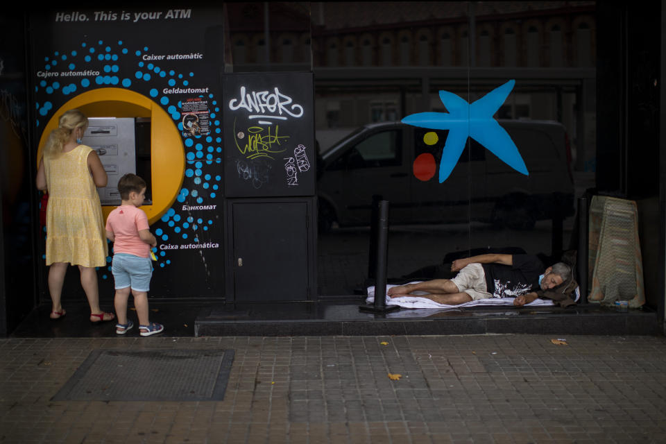 FILE, In this Friday July 17, 2020 file photo, a child looks at a man sleeping outside a CaixaBank brach office in Barcelona, Spain. Two of Spain's biggest banks are poised to merge and create the country's largest bank in terms of domestic operations, with assets of more than 600 billion euros (dollars 708 billion). The deal brings the prospect of more job losses amid difficult times for the financial sector. A tie-up between CaixaBank, the largest bank in the domestic market, and Bankia, Spain's biggest mortgage lender, could herald other moves toward consolidation in the financial sector. (AP Photo/Emilio Morenatti)