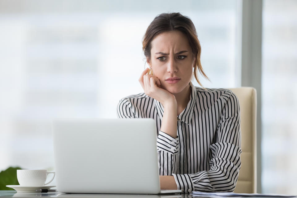 Confused businesswoman annoyed by spam email looking at laptop.