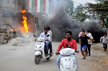 Men make their way past a burning lorry in Bengaluru, which was set on fire by protesters after Supreme Court ordered Karnataka to release 12,000 cubic feet of water per second every day from the Cauvery river to neighbouring Tamil Nadu, India September 12, 2016. REUTERS/Abhishek N. Chinnappa