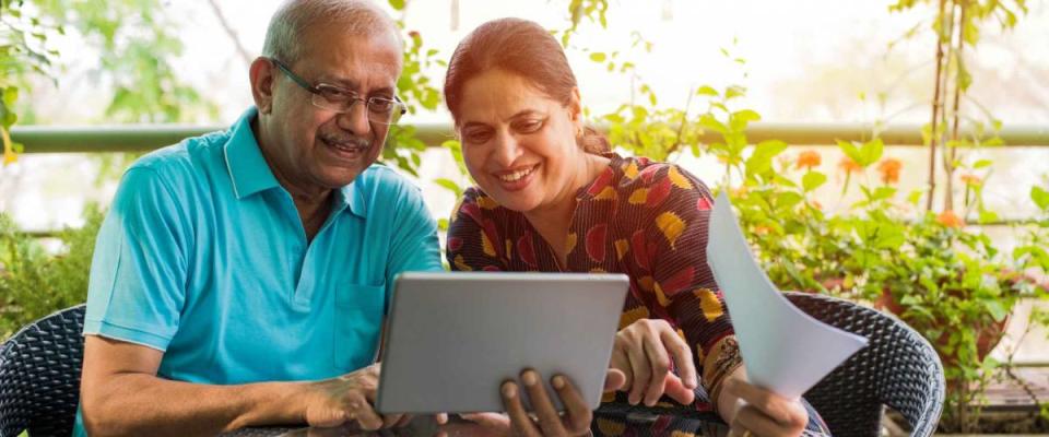 Senior Indian/asian couple accounting, doing home finance and checking bills with laptop, calculator and money while sitting on sofa/couch or dining table at home