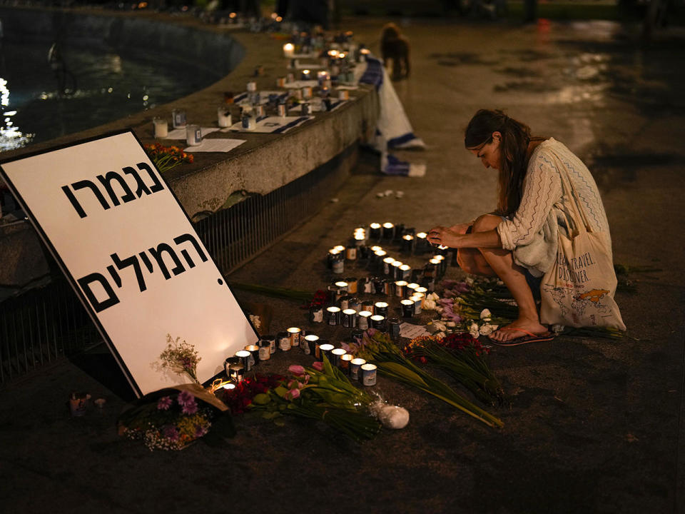 A woman lights candles in honor of victims of the Hamas attacks, in Dizengoff Square, Tel Aviv, Oct. 13, 2023. The writing reads: 