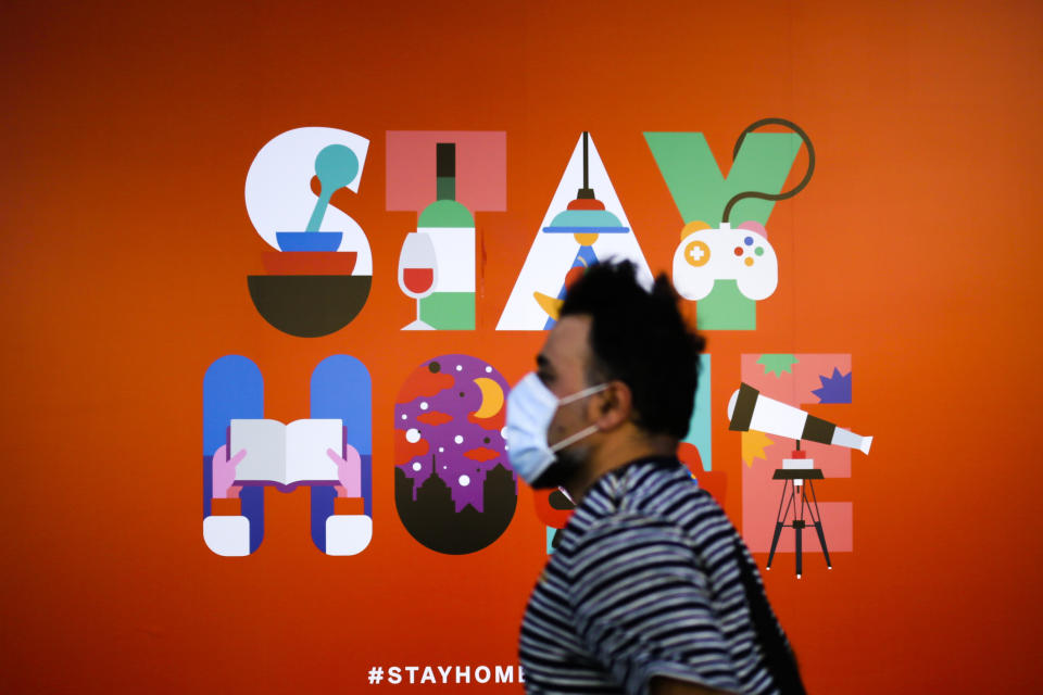 A man wearing a face mask walks in front of a poster recommending people to stay at home, at a department store in Berlin, Germany, Monday, April 20, 2020. Europe's biggest economy, starts reopening some of its stores and factories in parts of the country after weeks of lockdown due to the new coronavirus outbreak. (AP Photo/Markus Schreiber)