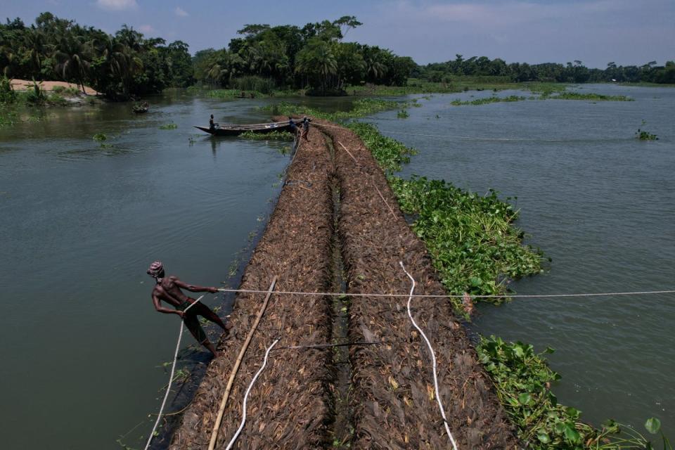 A man holds a rope as people transport floating beds towards a farm through the Belua river (Reuters)
