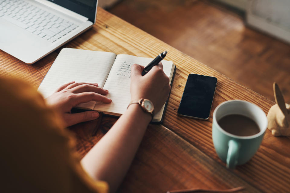 Someone writes a list in a notebook on a wooden table