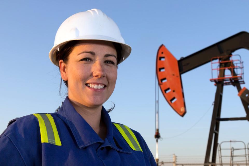 A person in protective gear with an oil well in the background.
