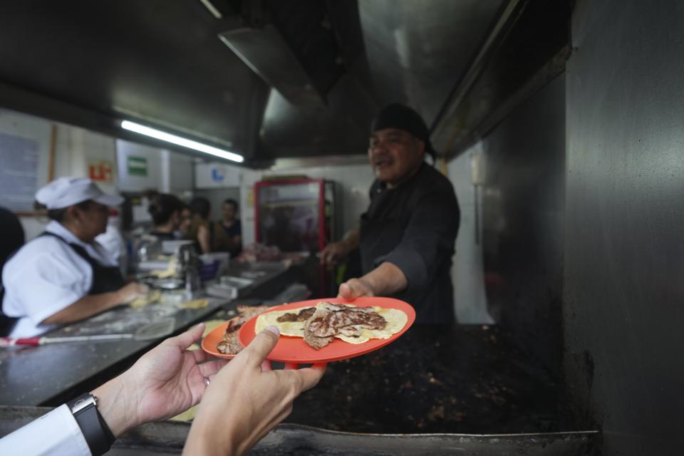 El chef Arturo Rivera Martínez, recién galardonado con una estrella Michelin, entrega una orden de tacos a un cliente en la taquería Tacos El Califa de León en Ciudad de México, el miércoles 15 de mayo de 2024. Tacos El Califa de León es la primera taquería en recibir una estrella Michelin. (AP Foto/Fernando Llano)