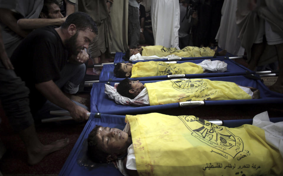 Fotografía de archivo del 16 de julio de 2014 de palestinos llorando frente a los cuerpos de cuatro niños de la familia Bakr, cubiertos con banderas amarillas del movimiento Fatah, durante su funeral en una mezquita en Ciudad de Gaza. (AP Foto/Khalil Hamra, Archivo)