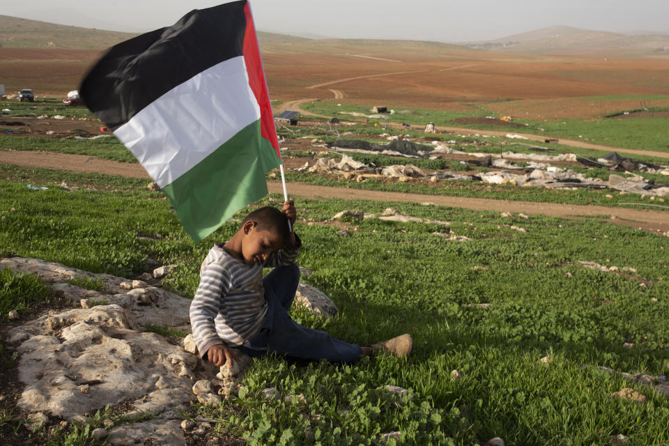 A Palestinian Bedouin boy holds a Palestinian flag after Israeli troops demolished tents and other structures of the Khirbet Humsu hamlet in the Jordan Valley in the West Bank, Wednesday, Feb. 3, 2021. A battle of wills is underway in the occupied West Bank, where Israel has demolished the herding community of Khirbet Humsu three times in as many months, displacing dozens of Palestinians. Each time they have returned and tried to rebuild, saying they have nowhere else to go. (AP Photo/Maya Alleruzzo)