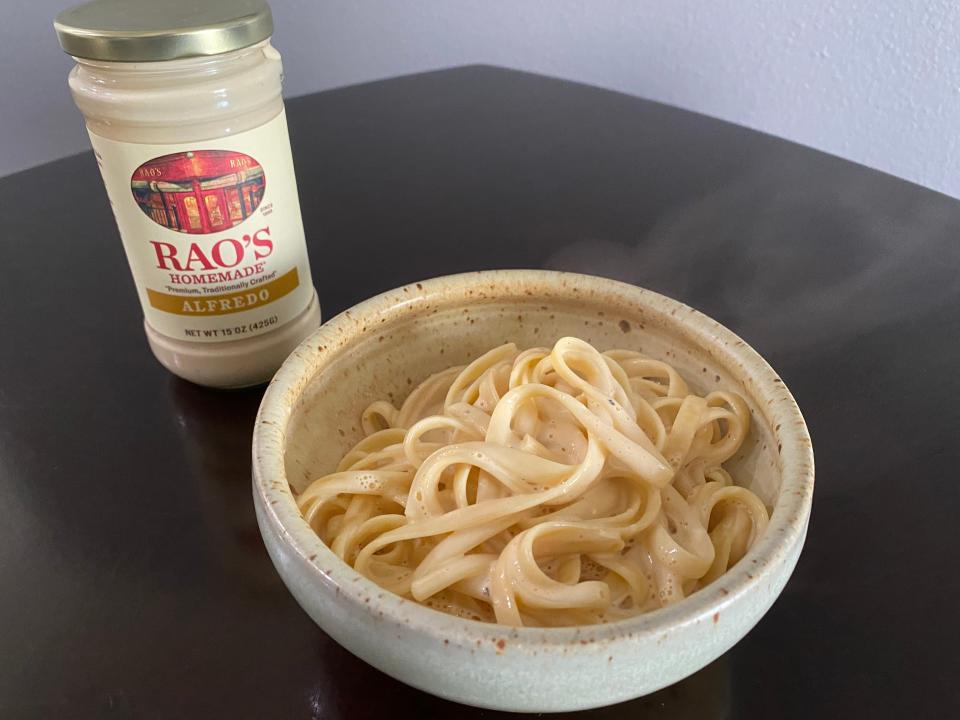 Bowl of Alfredo on black table with jar of Rao's Alfredo sauce in background