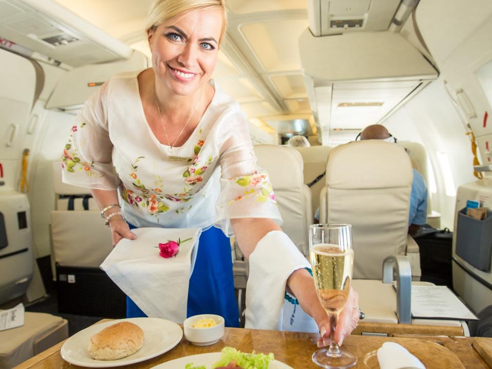 A flight attendant serving a drink to a table with salad, bread, and butter.